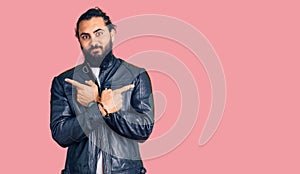 Young arab man wearing casual leather jacket pointing to both sides with fingers, different direction disagree