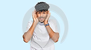 Young arab man wearing casual white t shirt trying to hear both hands on ear gesture, curious for gossip