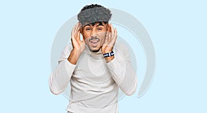 Young arab man wearing casual winter sweater trying to hear both hands on ear gesture, curious for gossip