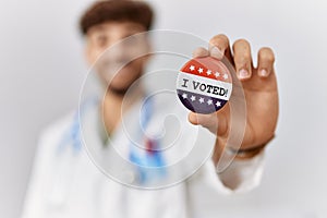 Young arab man wearing doctor uniform holding i voted badge at electoral college