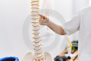 Young arab man wearing physiotherapist uniform pointing with finger to vertebra at clinic