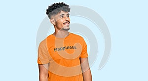 Young arab man wearing tshirt with happiness word message looking away to side with smile on face, natural expression