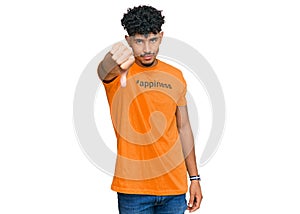 Young arab man wearing tshirt with happiness word message looking unhappy and angry showing rejection and negative with thumbs