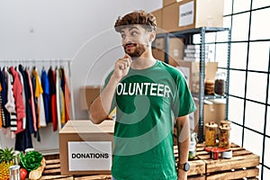 Young arab man wearing volunteer t shirt at donations stand looking confident at the camera smiling with crossed arms and hand