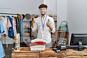 Young arab man working as manager at retail boutique holding alarm tag smiling happy and positive, thumb up doing excellent and