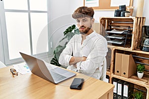 Young arab man working using computer laptop at the office skeptic and nervous, disapproving expression on face with crossed arms