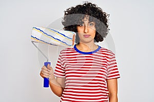 Young arab painter woman with curly hair holding paint roller over isolated white background with a confident expression on smart