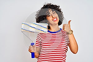 Young arab painter woman with curly hair holding paint roller over isolated white background happy with big smile doing ok sign,