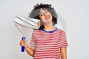 Young arab painter woman with curly hair holding paint roller over isolated white background with a happy face standing and