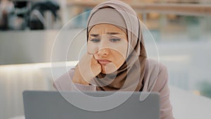 Young arab sorrowful woman in hijab reading message on laptop gets bad news denied bank loan job dismissal bankruptcy