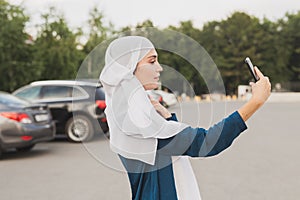 Young Arab student girl wearing a headscarf making selfie on her smartphone outdoors.