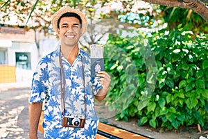 Young arab tourist man using vintage camera holding canadian passport and boarding pass at the park