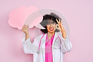 Young arab woman with curly hair holding cloud speech bubble over isolated pink background doing ok sign with fingers, excellent