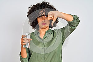 Young arab woman with curly hair holding glass of water over isolated white background with angry face, negative sign showing