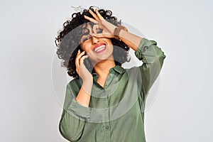 Young arab woman with curly hair talking on smartphone over isolated white background with happy face smiling doing ok sign with