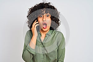 Young arab woman with curly hair talking on smartphone over isolated white background scared in shock with a surprise face, afraid