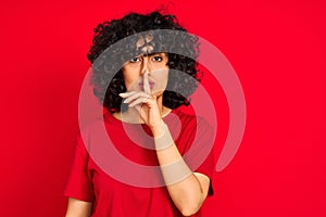 Young arab woman with curly hair wearing casual t-shirt over isolated red background asking to be quiet with finger on lips