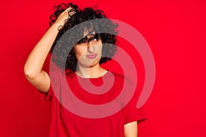 Young arab woman with curly hair wearing casual t-shirt over isolated red background confuse and wonder about question