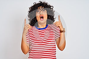 Young arab woman with curly hair wearing striped t-shirt over isolated white background amazed and surprised looking up and