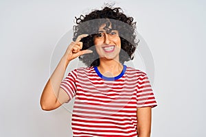Young arab woman with curly hair wearing striped t-shirt over isolated white background smiling and confident gesturing with hand