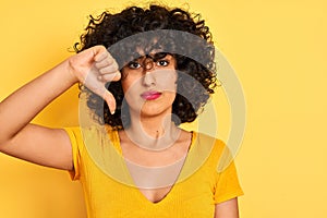 Young arab woman with curly hair wearing t-shirt standing over isolated yellow background with angry face, negative sign showing