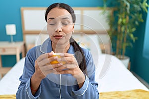 Young arab woman drinking cup of coffee sitting on bed at bedroom