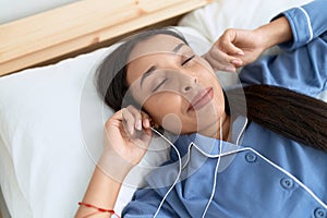 Young arab woman listening to music lying on bed at bedroom