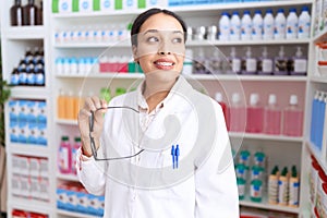 Young arab woman pharmacist smiling confident holding glasses at pharmacy