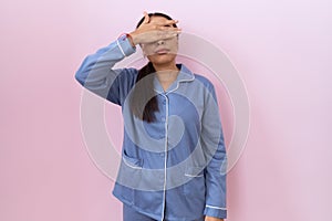 Young arab woman wearing blue pajama covering eyes with hand, looking serious and sad