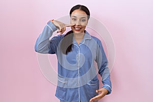 Young arab woman wearing blue pajama pointing with hand finger to face and nose, smiling cheerful