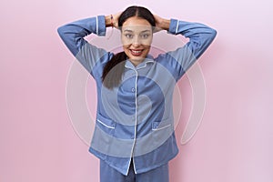 Young arab woman wearing blue pajama relaxing and stretching, arms and hands behind head and neck smiling happy