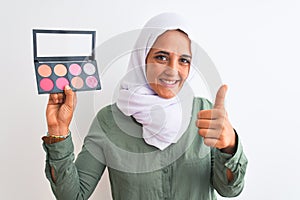 Young Arab woman wearing hijab showing makeup blush palette over isolated background happy with big smile doing ok sign, thumb up