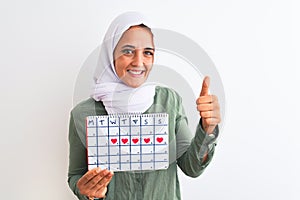 Young Arab woman wearing hijab showing menstruation calendar over isolated background happy with big smile doing ok sign, thumb up