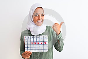 Young Arab woman wearing hijab showing menstruation calendar over isolated background pointing and showing with thumb up to the