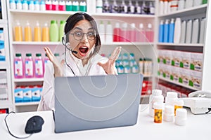 Young arab woman working at pharmacy drugstore using laptop celebrating crazy and amazed for success with arms raised and open