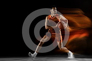 Young arabian basketball player of team in action, motion isolated on black background in mixed light. Concept of sport