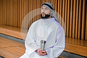 Young arabian man sitting on a wooden bench with metal cup