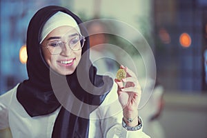 Young arabian muslim woman in hijab black clothes hold in hand holding bitcoin. C