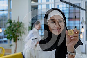 Young arabian muslim woman in hijab black clothes hold in hand holding bitcoin. C