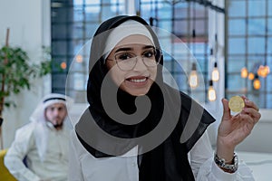 Young arabian muslim woman in hijab black clothes hold in hand holding bitcoin. C