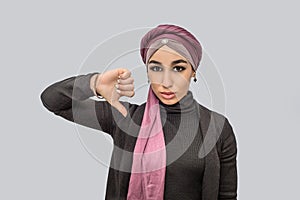 Young arabian woman stand and hlold big thumb down. She looks on camera. Model is serious. She wears hidjab and black