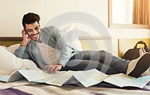 Young arabic man traveller lying on bed and studying map