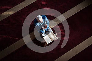 Young Arabic Muslim man reading Koran and praying. Religious muslim man reading holy koran inside the mosque