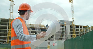 Young architect or builder With Hard Hat Holding Blueprint In His Hands in front of building under construction. Close