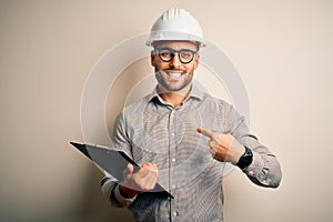 Young architect inspector man wearing builder safety helmet and using clipboard with surprise face pointing finger to himself