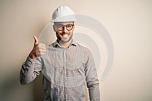 Young architect man wearing builder safety helmet over isolated background doing happy thumbs up gesture with hand