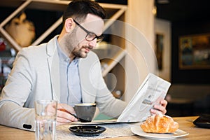 Young architect reading newspapers and drinking coffee in a modern cafe. Work anywhere concept