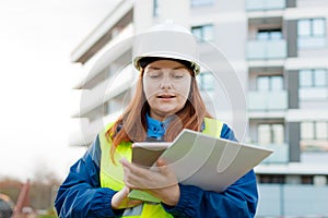 Young architect woman in white hardhat and safety vest using digital tablet outdoors. Female construction engineer