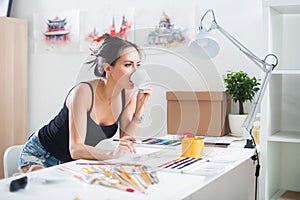 Young artist drawing watercolor picture sideview, holding cup of coffee photo