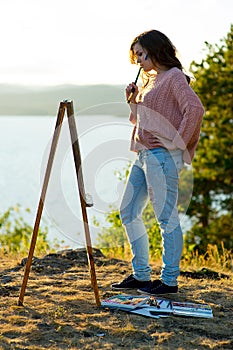 Young artist draws a seascape at sunset